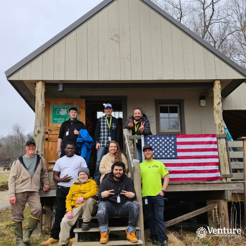 Venture Community Services staff and program participants posing outside a rustic program building