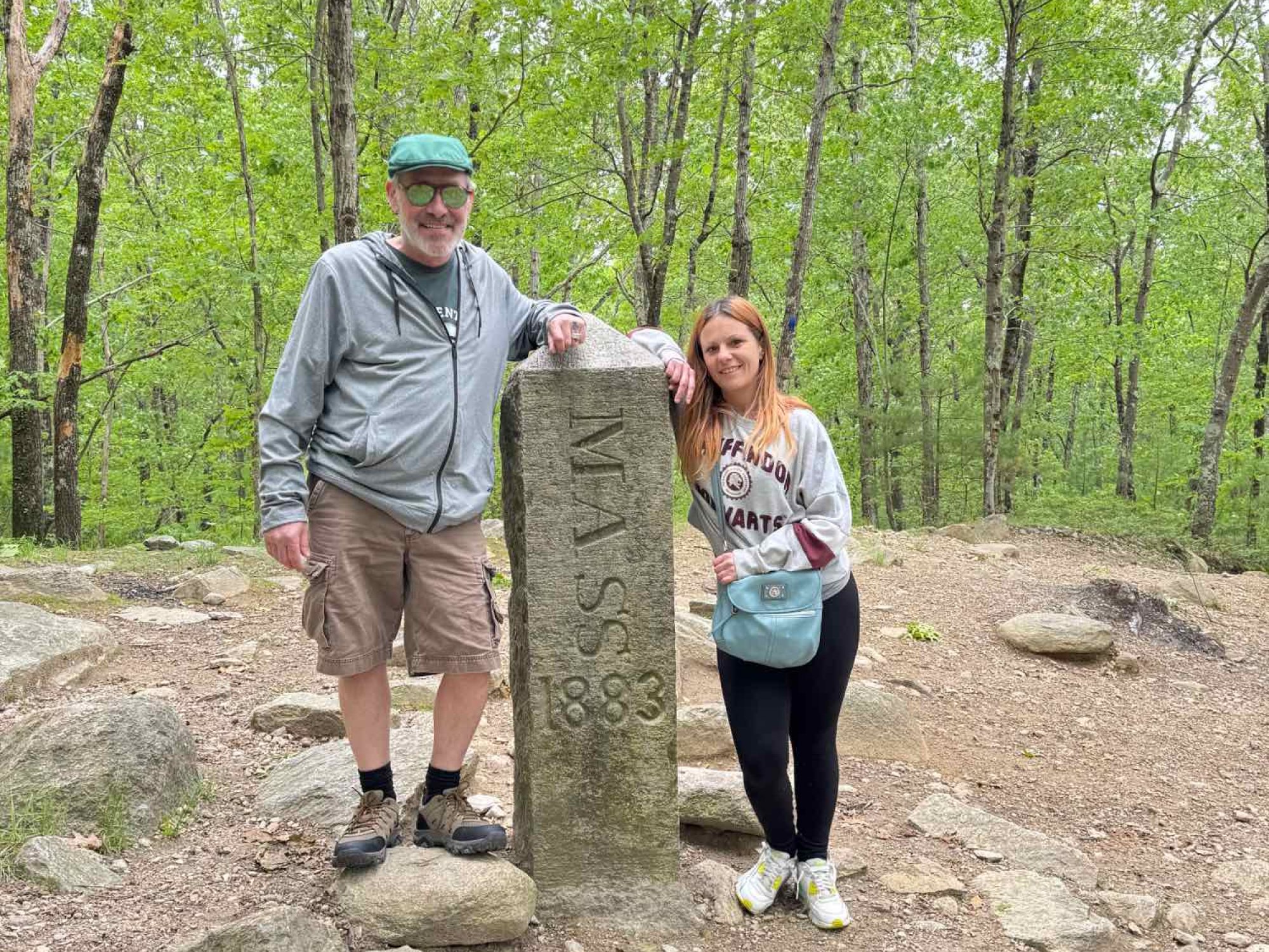 Two people posing next to a Massachusetts state boundary marker during an outdoor community outing