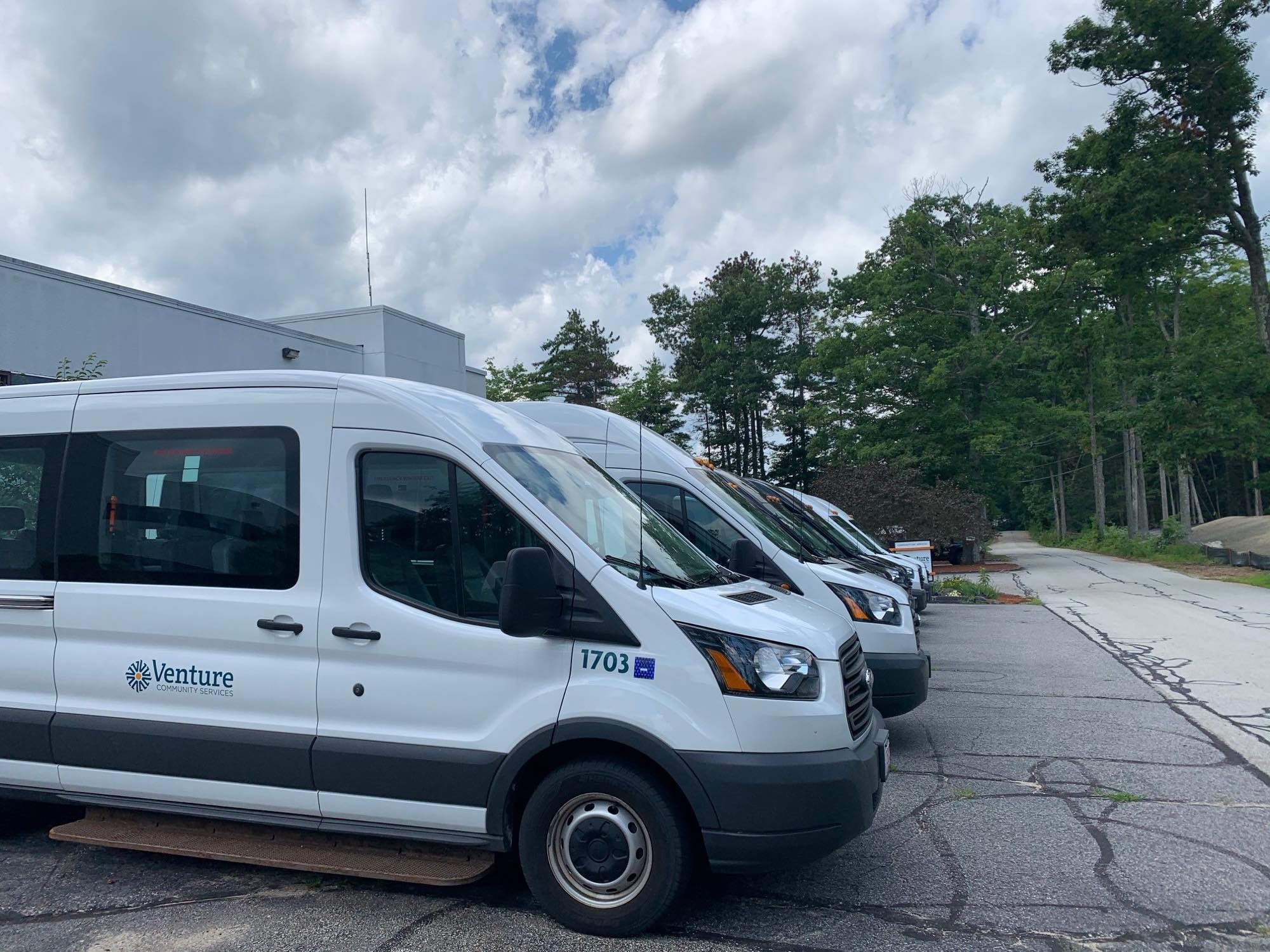 A row of white Venture Community Services transport vans parked outside a facility