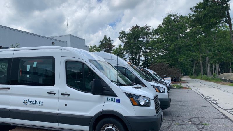 A row of white Venture Community Services transport vans parked outside a facility